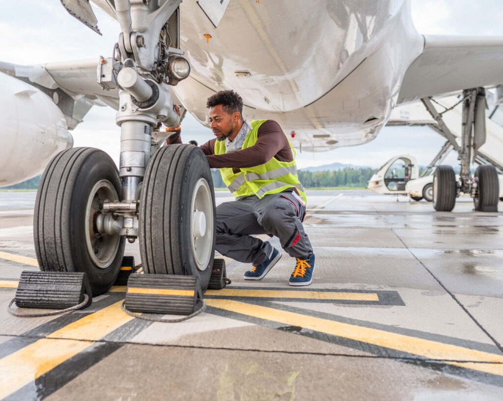 Handsome mid adult Hispanic male employee working under an aircraft. He is checking the wheels and wearing a reflective vest.